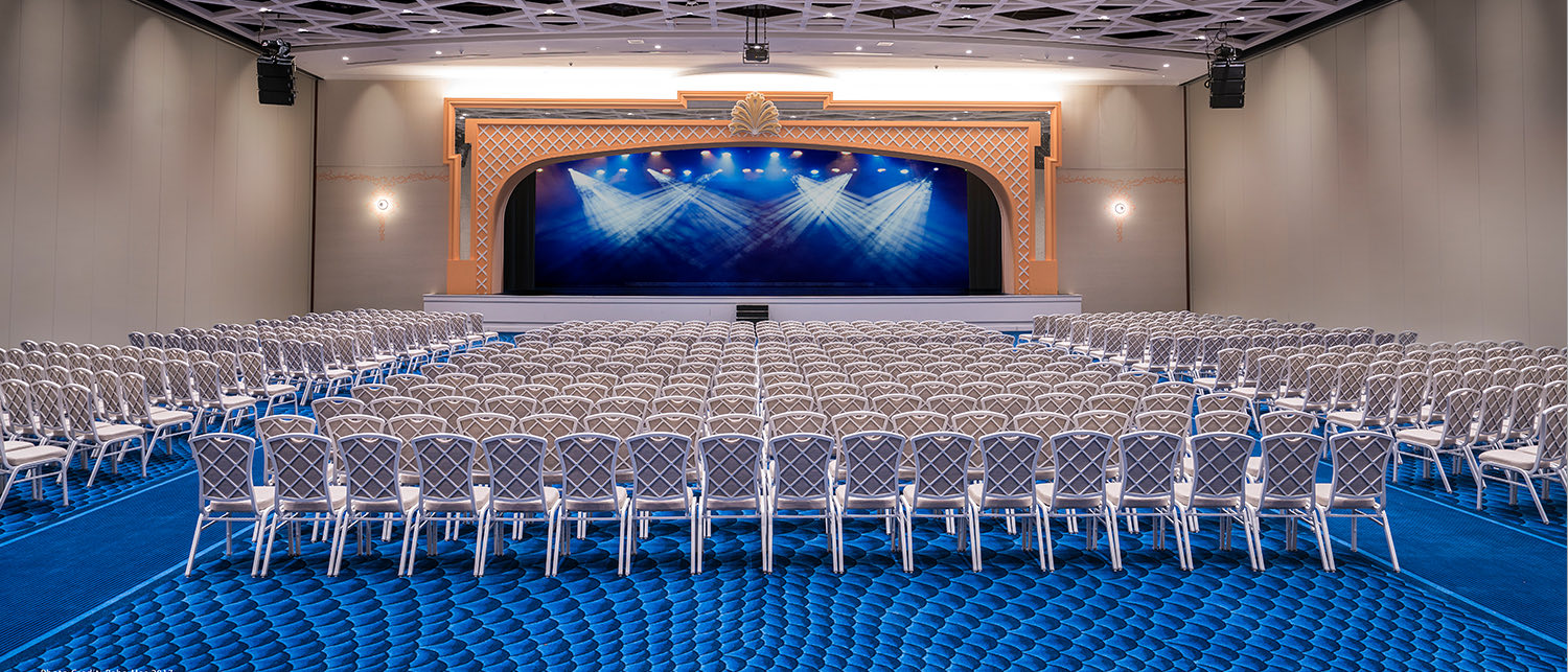 Large Event room with blue carpet, chairs and large stage at the center