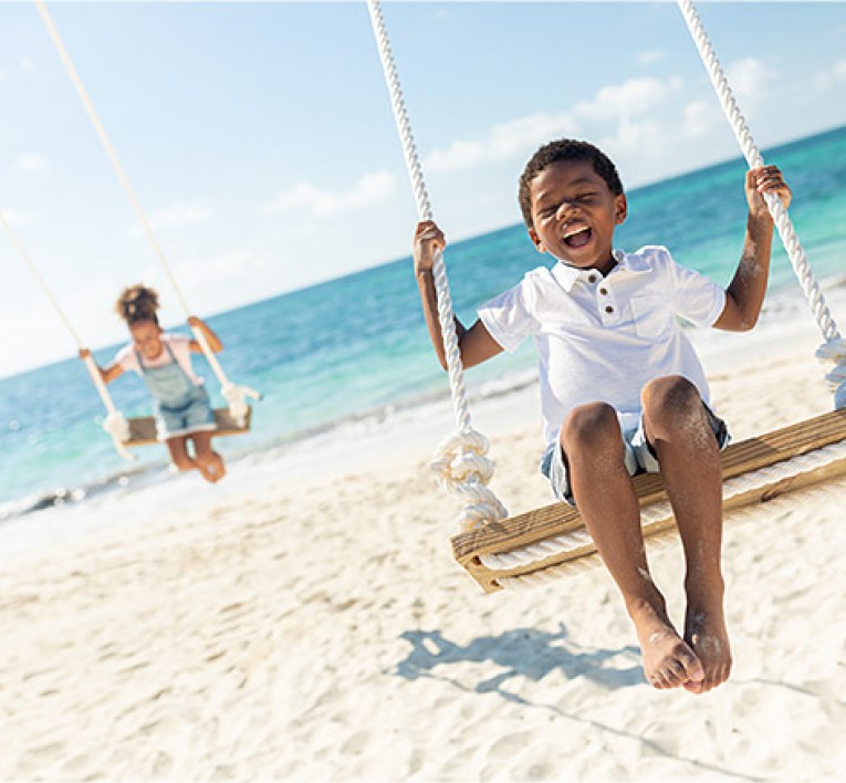 Young Boy And Girl On Swings At The Beach